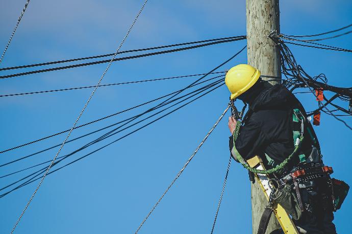 man in black jacket and yellow hard hat climbing on brown wooden post during daytime